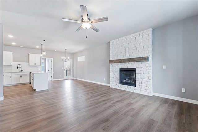 unfurnished living room featuring light hardwood / wood-style flooring, sink, ceiling fan with notable chandelier, and a fireplace