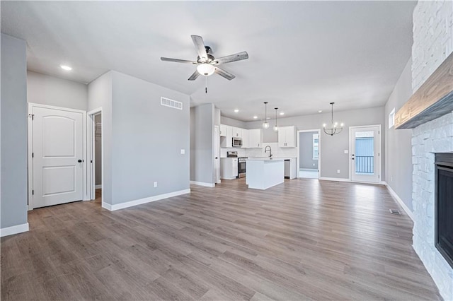 unfurnished living room with light hardwood / wood-style flooring, sink, a stone fireplace, and ceiling fan with notable chandelier