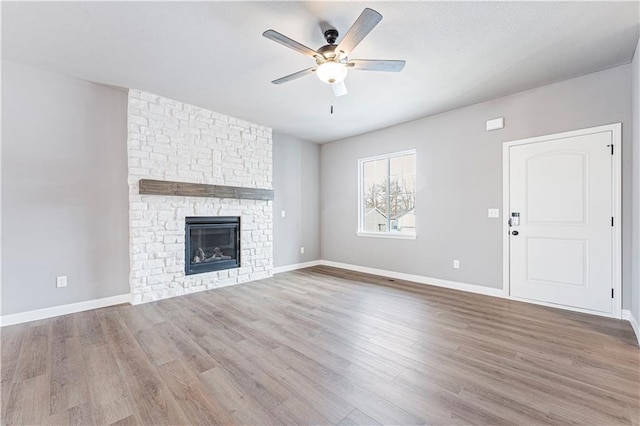 unfurnished living room with a stone fireplace, light hardwood / wood-style flooring, and ceiling fan