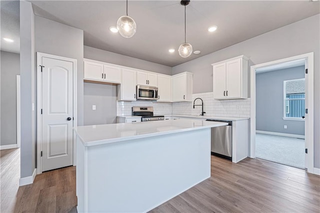 kitchen with appliances with stainless steel finishes, decorative light fixtures, white cabinets, a center island, and light hardwood / wood-style flooring