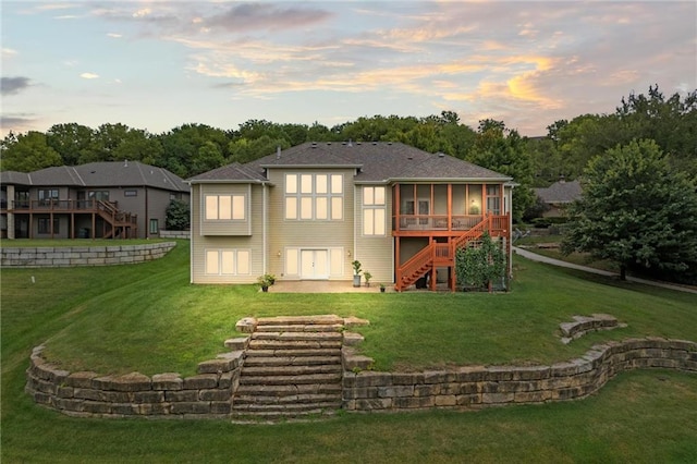 back house at dusk with a sunroom, a lawn, and a wooden deck