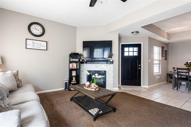 carpeted living area with tile patterned floors, baseboards, a stone fireplace, and ceiling fan