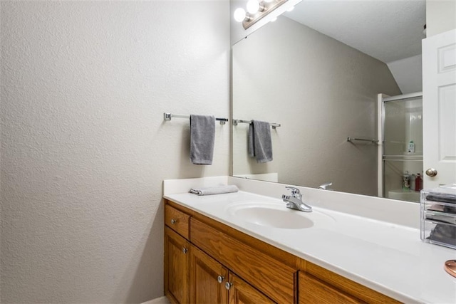 bathroom with an enclosed shower, vaulted ceiling, vanity, and a textured wall