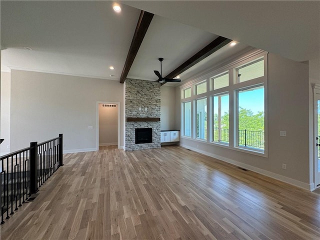 unfurnished living room featuring light hardwood / wood-style floors, beam ceiling, a fireplace, crown molding, and ceiling fan