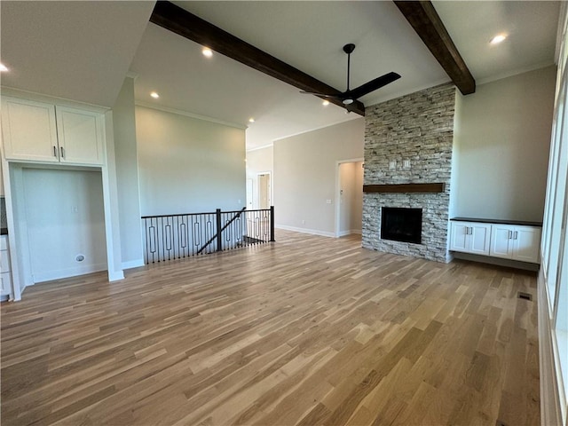 unfurnished living room featuring beamed ceiling, light wood-style floors, ceiling fan, a stone fireplace, and baseboards