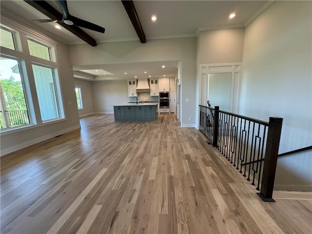unfurnished living room with light wood-type flooring, beam ceiling, and baseboards