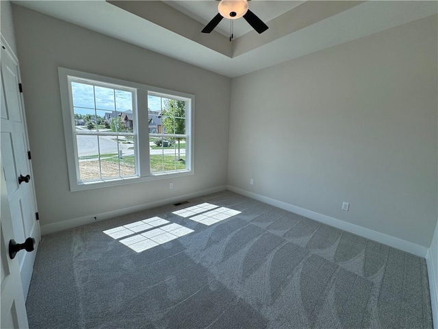spare room with a raised ceiling, a ceiling fan, visible vents, baseboards, and carpet floors