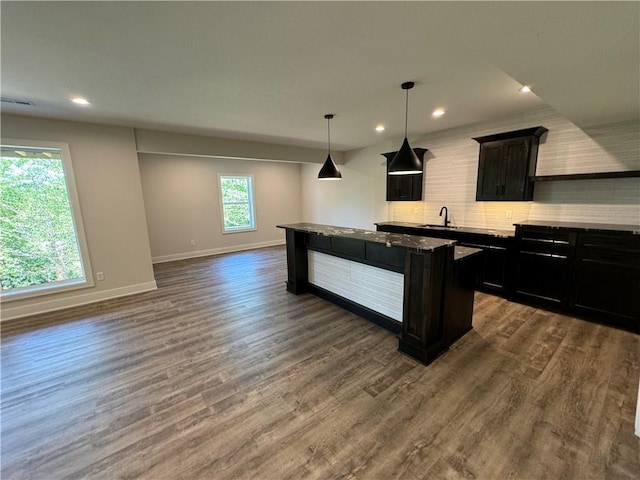 kitchen featuring decorative backsplash, a sink, a kitchen island, baseboards, and recessed lighting
