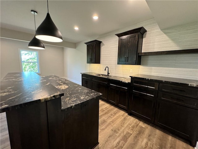 kitchen featuring dark stone countertops, tasteful backsplash, a sink, a center island, and light wood-type flooring