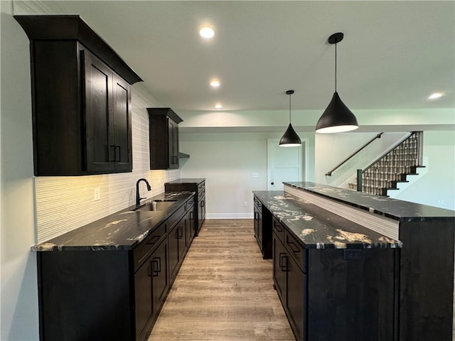 kitchen featuring dark stone countertops, light wood-style flooring, decorative backsplash, a sink, and a center island