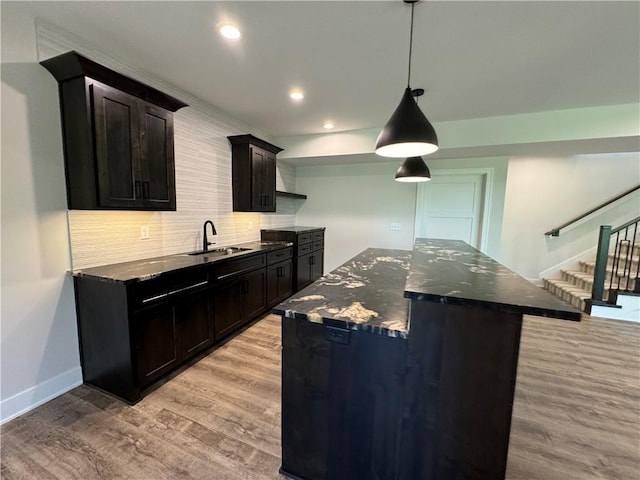 kitchen with dark stone counters, decorative backsplash, a center island, a sink, and light wood-type flooring