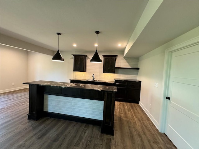 kitchen featuring dark wood-style floors, a sink, a center island, backsplash, and baseboards