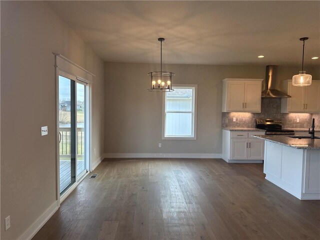 kitchen with wall chimney exhaust hood, stainless steel range with electric cooktop, hanging light fixtures, decorative backsplash, and white cabinets