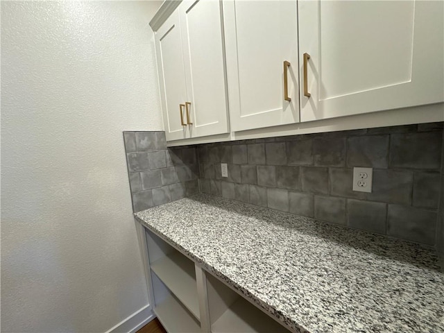 interior space with white cabinetry, backsplash, and light stone countertops