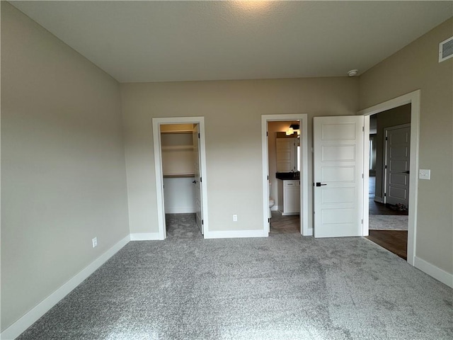 unfurnished bedroom with dark carpet, a walk in closet, ensuite bath, and a closet