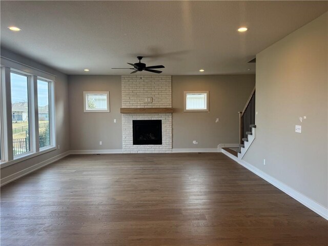 unfurnished living room featuring a brick fireplace, dark hardwood / wood-style floors, and ceiling fan