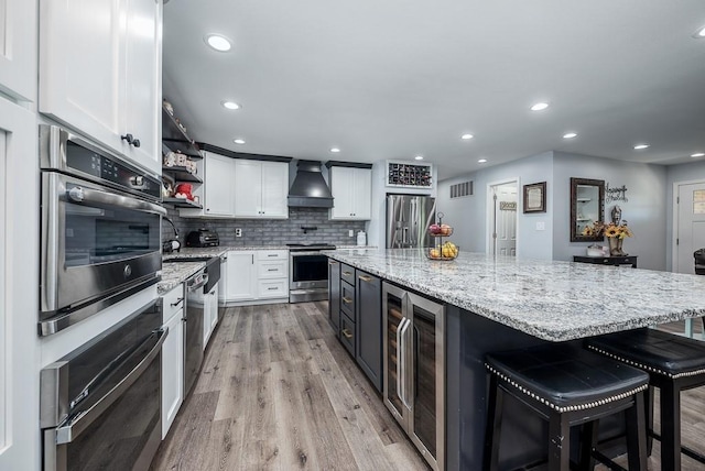 kitchen with appliances with stainless steel finishes, premium range hood, white cabinetry, a spacious island, and a breakfast bar area