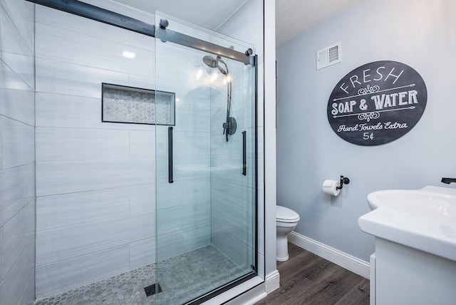 bathroom with hardwood / wood-style floors, toilet, vanity, and walk in shower