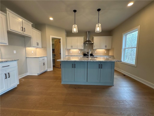 kitchen featuring wall chimney exhaust hood, sink, hanging light fixtures, an island with sink, and white cabinets