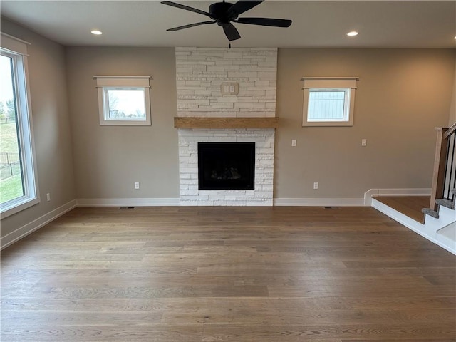 unfurnished living room with a stone fireplace, wood-type flooring, and ceiling fan