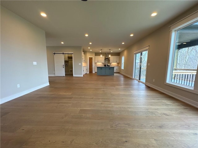 unfurnished living room with a barn door and light hardwood / wood-style flooring