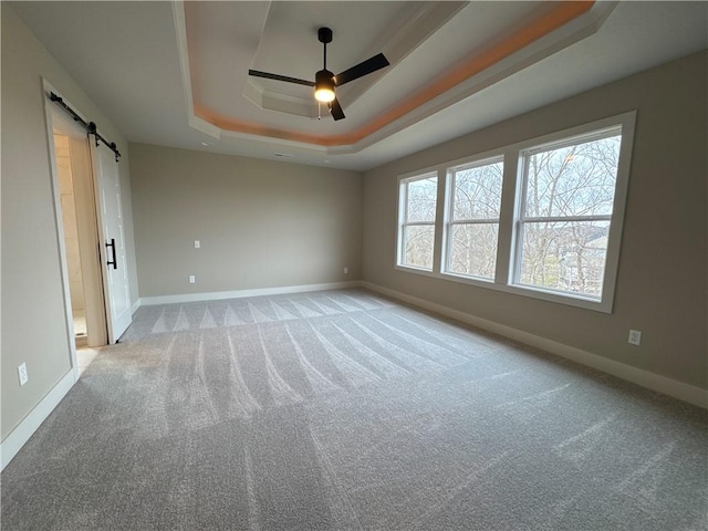 carpeted spare room featuring ceiling fan, a barn door, and a raised ceiling