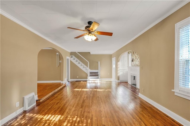 unfurnished living room featuring a brick fireplace, ornamental molding, hardwood / wood-style floors, and ceiling fan