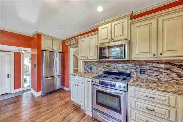 kitchen featuring decorative backsplash, light stone countertops, cream cabinetry, and appliances with stainless steel finishes