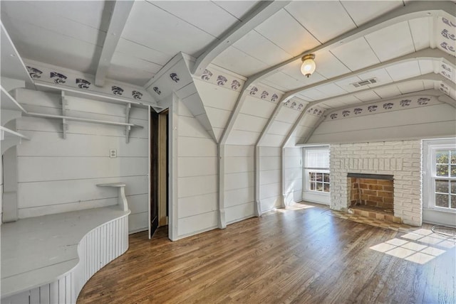 unfurnished living room featuring hardwood / wood-style floors, vaulted ceiling, a brick fireplace, and wood walls