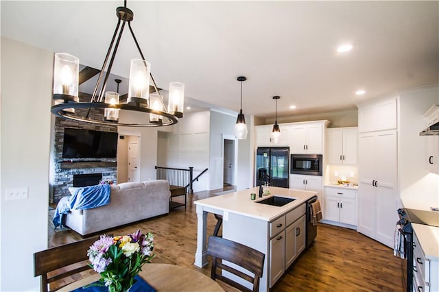 kitchen featuring a fireplace, black appliances, dark hardwood / wood-style flooring, an island with sink, and sink