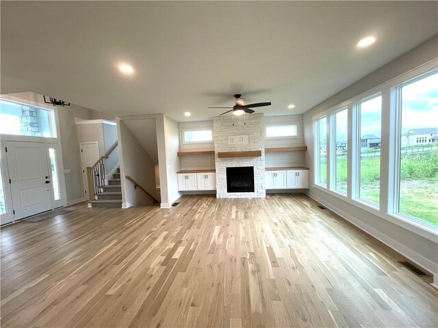 unfurnished living room featuring light hardwood / wood-style flooring, ceiling fan, and a stone fireplace