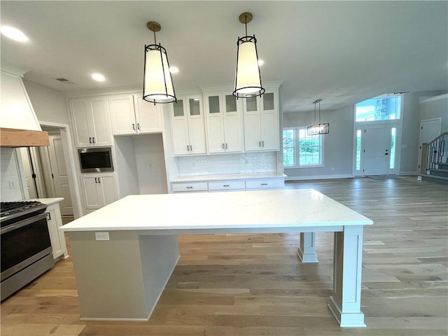 kitchen featuring a kitchen island, appliances with stainless steel finishes, light hardwood / wood-style floors, hanging light fixtures, and white cabinets