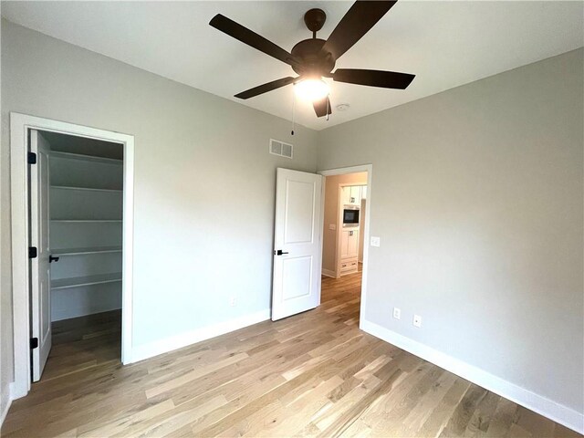 unfurnished bedroom featuring light hardwood / wood-style flooring, ceiling fan, a spacious closet, and a closet