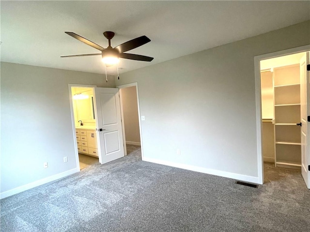 unfurnished bedroom featuring ceiling fan, ensuite bathroom, a spacious closet, and carpet floors