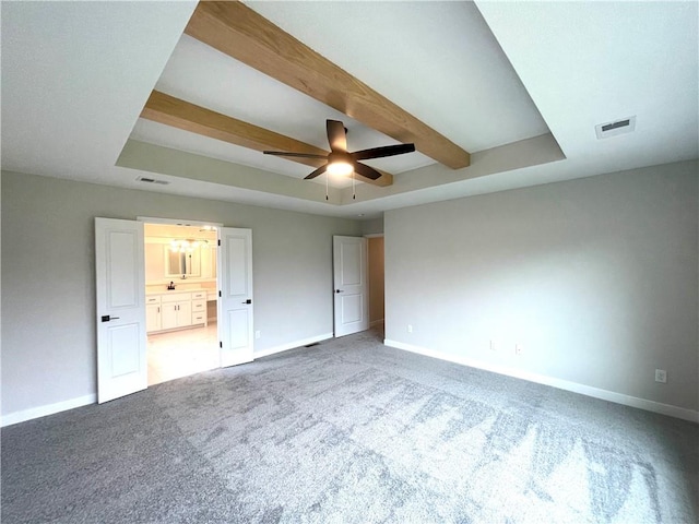 unfurnished bedroom with ensuite bathroom, carpet flooring, beamed ceiling, a raised ceiling, and ceiling fan