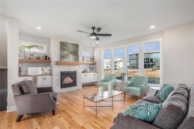 living room featuring a stone fireplace, recessed lighting, light wood-style floors, and ceiling fan