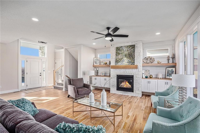 living area featuring light wood finished floors, a stone fireplace, a healthy amount of sunlight, and stairs