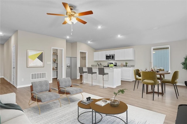 living room with ceiling fan, light hardwood / wood-style floors, and vaulted ceiling