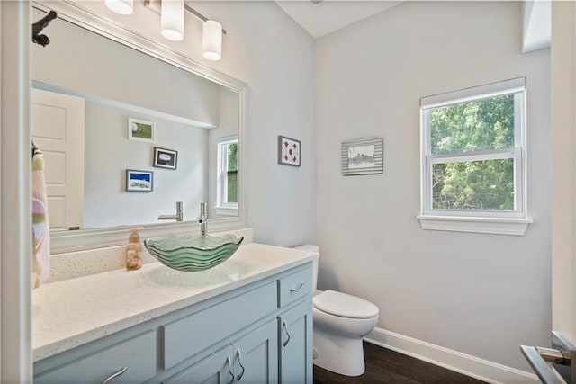 bathroom with toilet, wood finished floors, vanity, and baseboards