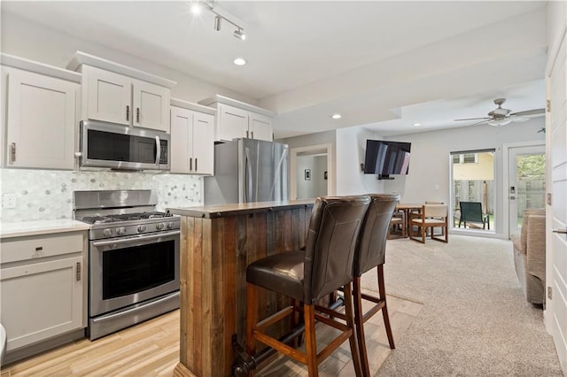 kitchen featuring tasteful backsplash, light countertops, appliances with stainless steel finishes, a kitchen breakfast bar, and a kitchen island