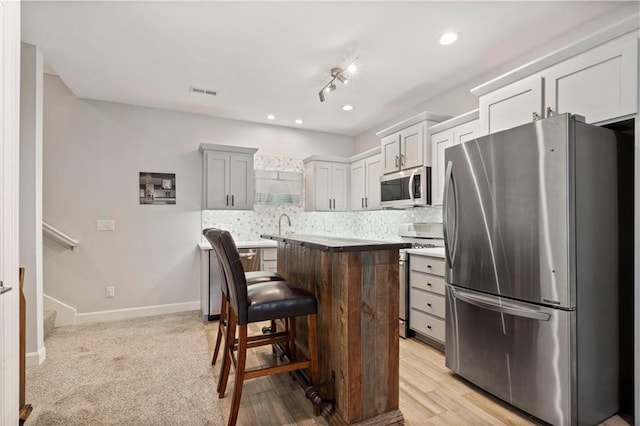 kitchen featuring a kitchen breakfast bar, a center island, stainless steel appliances, baseboards, and backsplash
