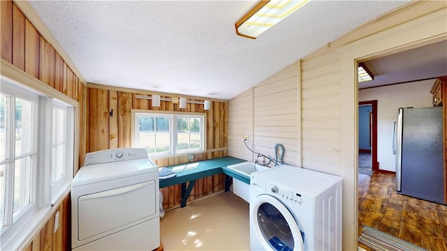 laundry room with hardwood / wood-style floors, a textured ceiling, washing machine and clothes dryer, wood walls, and sink