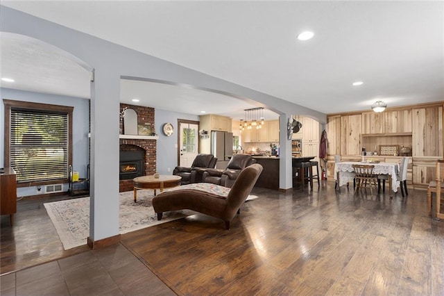 living room featuring dark wood-type flooring, a chandelier, and a fireplace