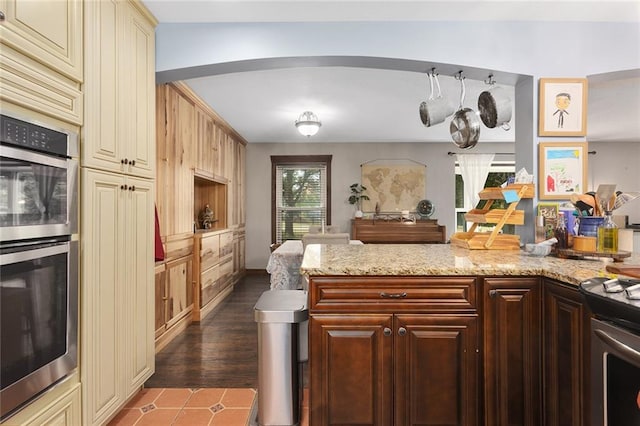 kitchen with dark brown cabinets, stainless steel appliances, light stone countertops, cream cabinets, and dark wood-type flooring