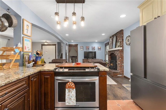 kitchen featuring a fireplace, light wood-type flooring, stainless steel appliances, light stone countertops, and dark brown cabinetry