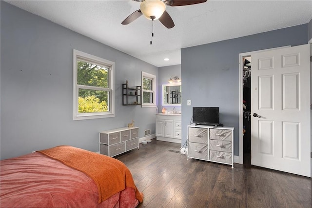 bedroom featuring a spacious closet, a closet, dark wood-type flooring, ensuite bath, and ceiling fan