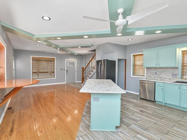 kitchen featuring blue cabinetry, tasteful backsplash, stainless steel appliances, light wood-style floors, and light countertops