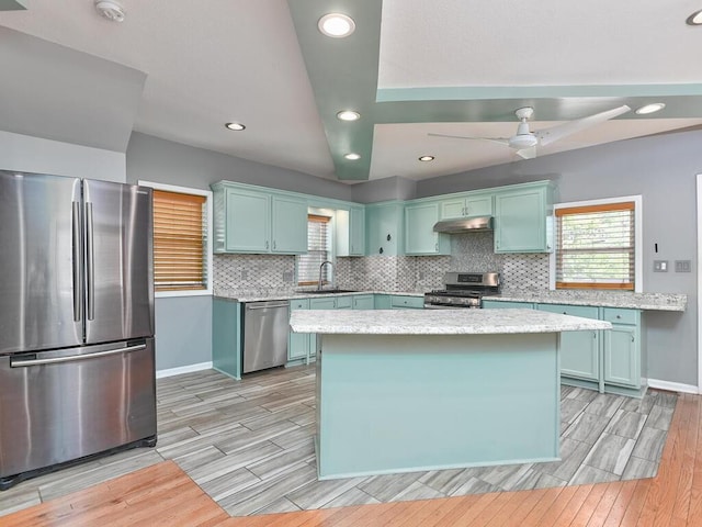 kitchen featuring wood finish floors, a sink, decorative backsplash, stainless steel appliances, and under cabinet range hood