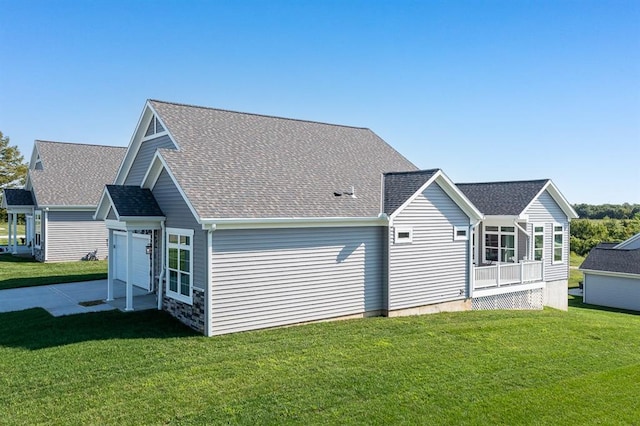 back of property featuring a garage, a shingled roof, and a lawn