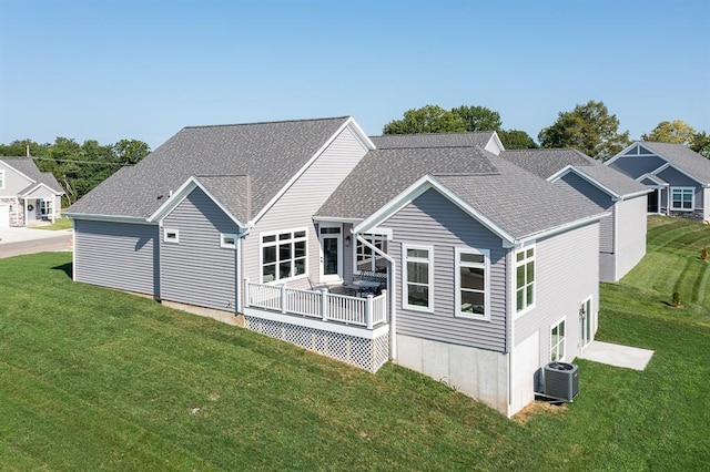 rear view of house with central AC unit, a lawn, and roof with shingles